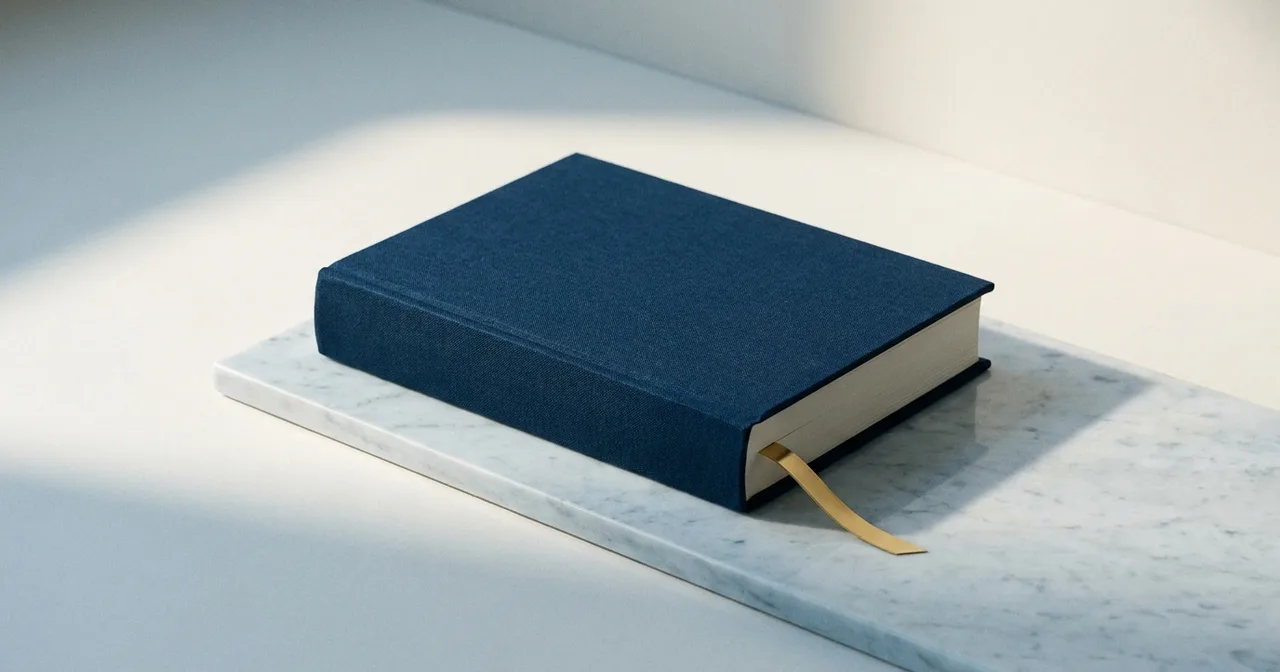 Livre relié de toile bleu marine, dos vierge, posé sur une dalle de marbre clair.