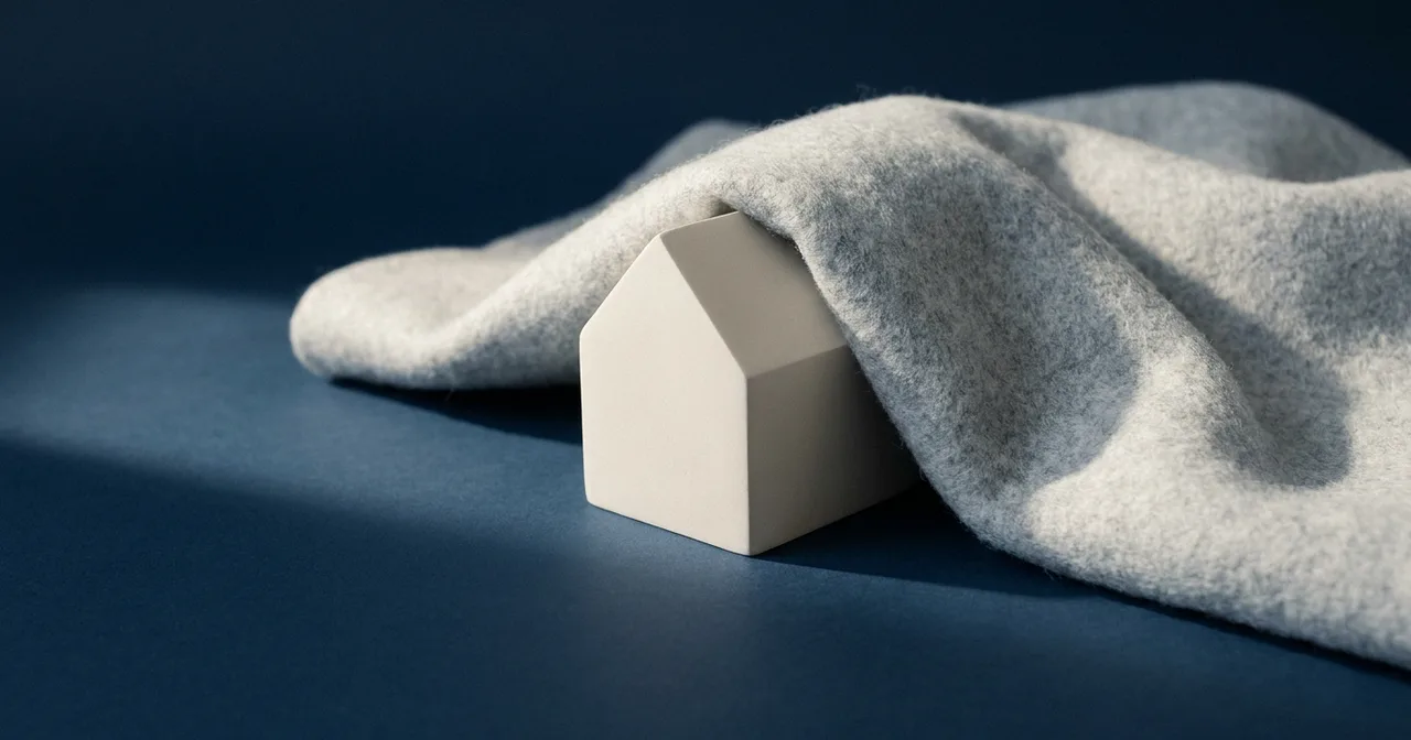 Maquette de maison blanche à demi enveloppée dans une couverture de feutre gris clair.